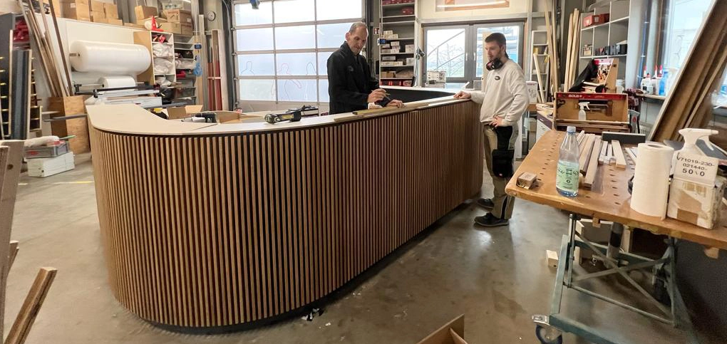 Zwei Schreiner prüfen eine geschwungene Theke in Lamellenoptik in der MTB Schreinerei in 68535 Edingen-Neckarhausen – individuelle Möbel nach Maß für Mannheim, Heidelberg, Weinheim und Umgebung.